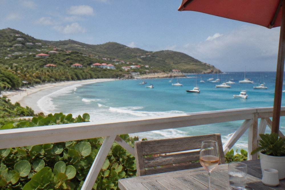 A red-roofed hotel terrace overlooking a bay with sailboats at anchor