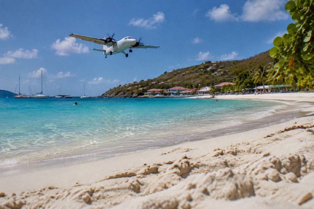 A small turboprop airplane descending low over a beach toward a short runway by the sea