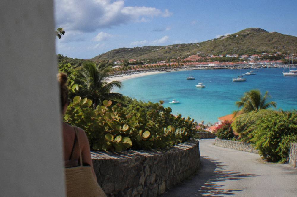 A hillside road winding past tropical vegetation with a view of a turquoise bay below