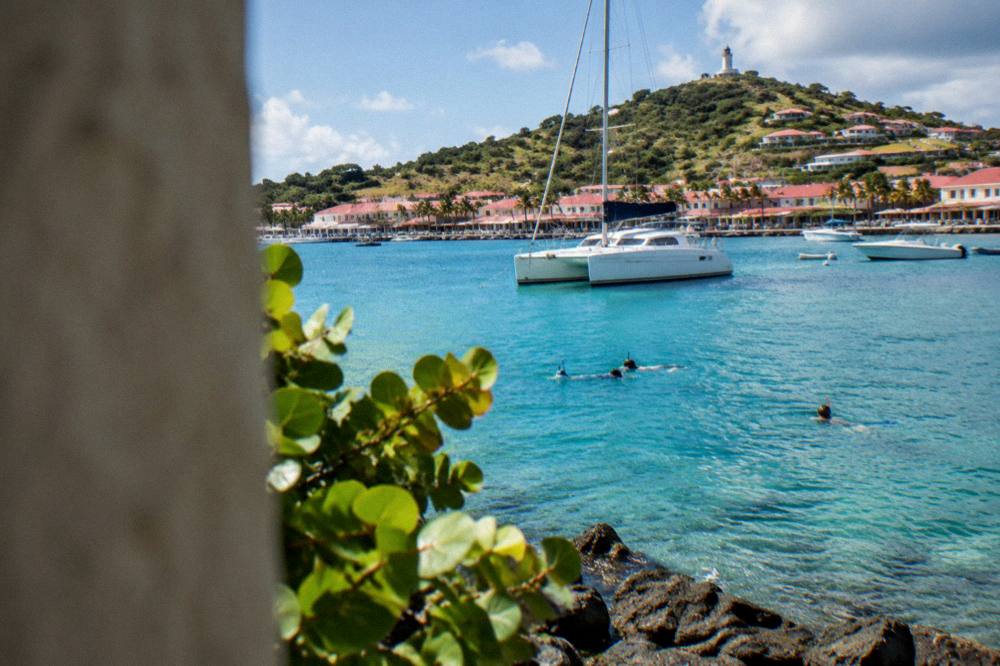 A catamaran anchored in a quiet Caribbean bay with snorkelers in the water near rocks