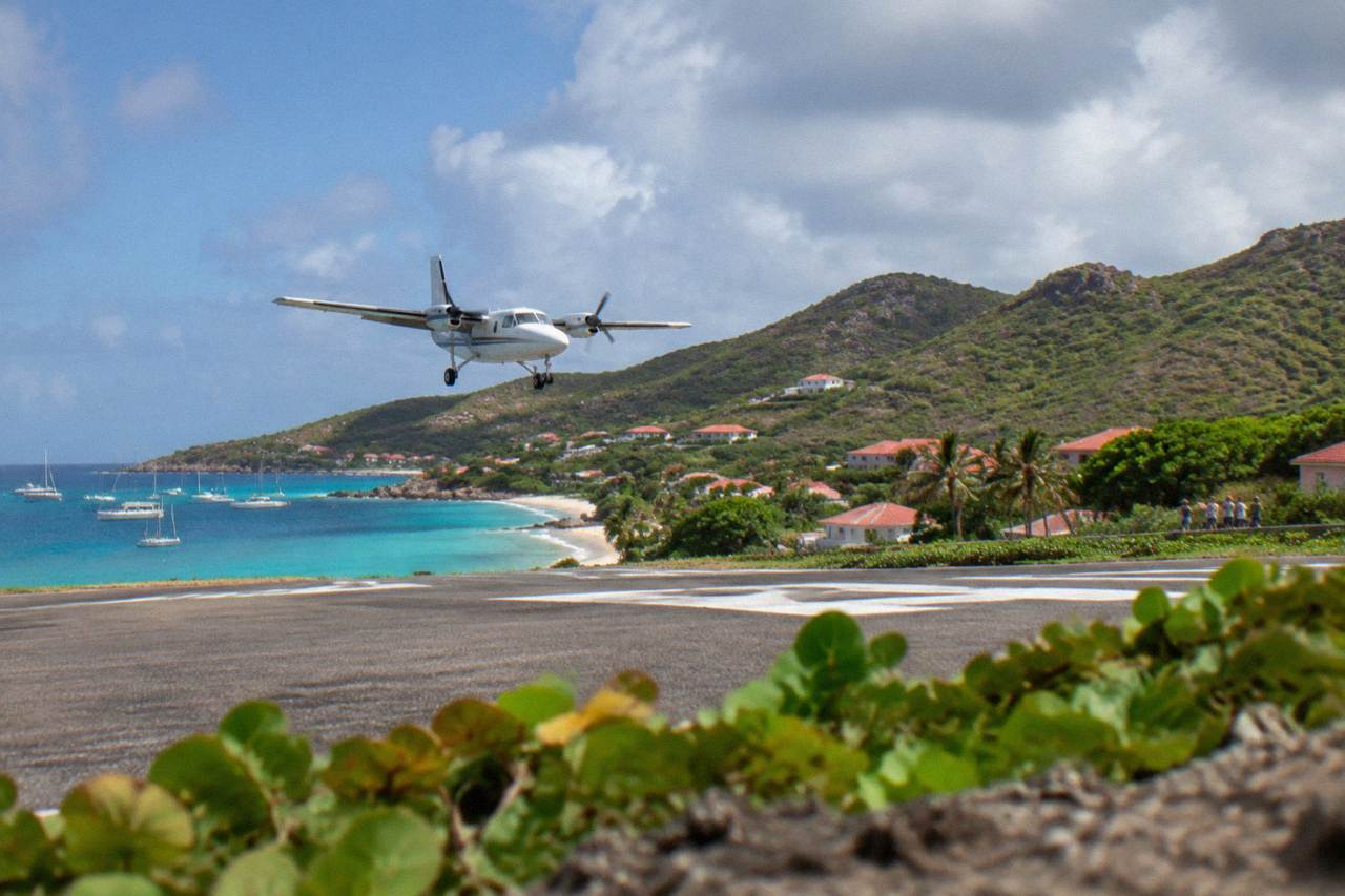 A small turboprop airplane on a short Caribbean runway with green hills behind it