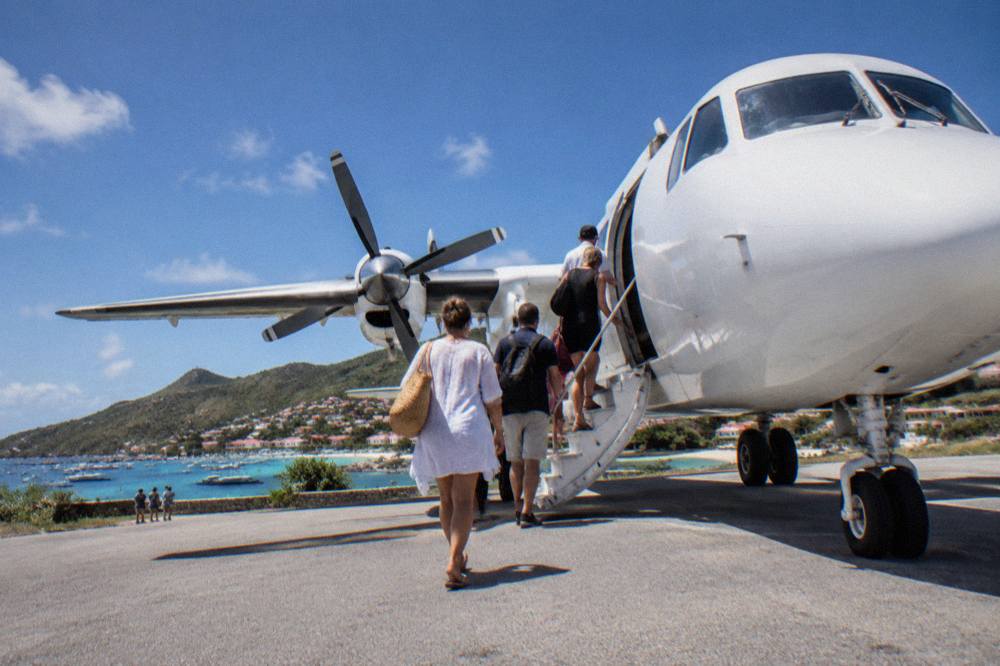 Passengers boarding a small white turboprop aircraft on a sunny Caribbean airstrip