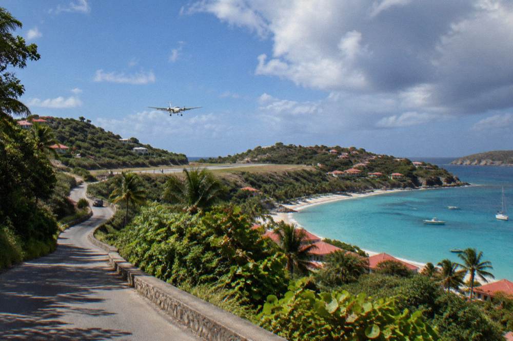 A narrow winding road climbing a green hill above a Caribbean bay