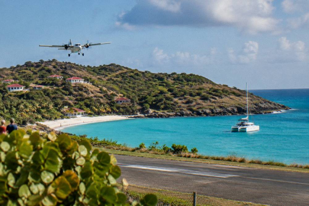 A white catamaran anchored in a clear turquoise bay with a wooded headland behind