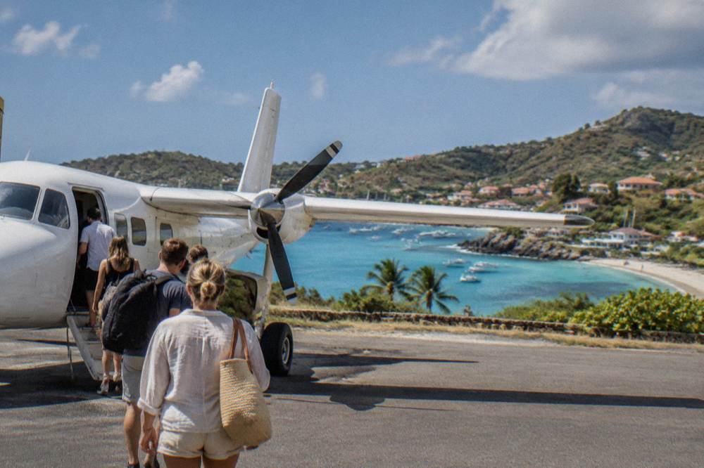 Passengers boarding a small eight-seat propeller plane on a sunny Caribbean airstrip