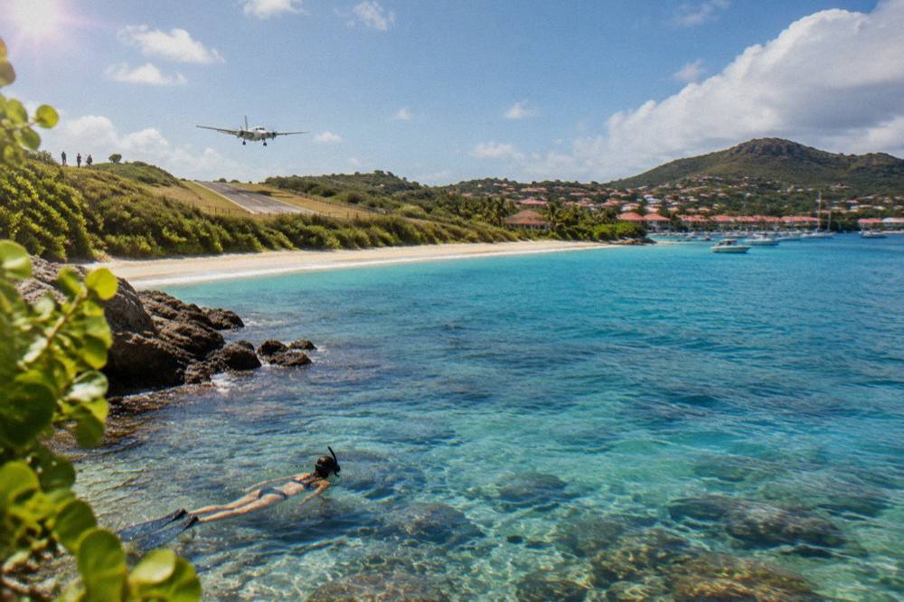 Snorkeler swimming over clear shallow water above rocks and small fish