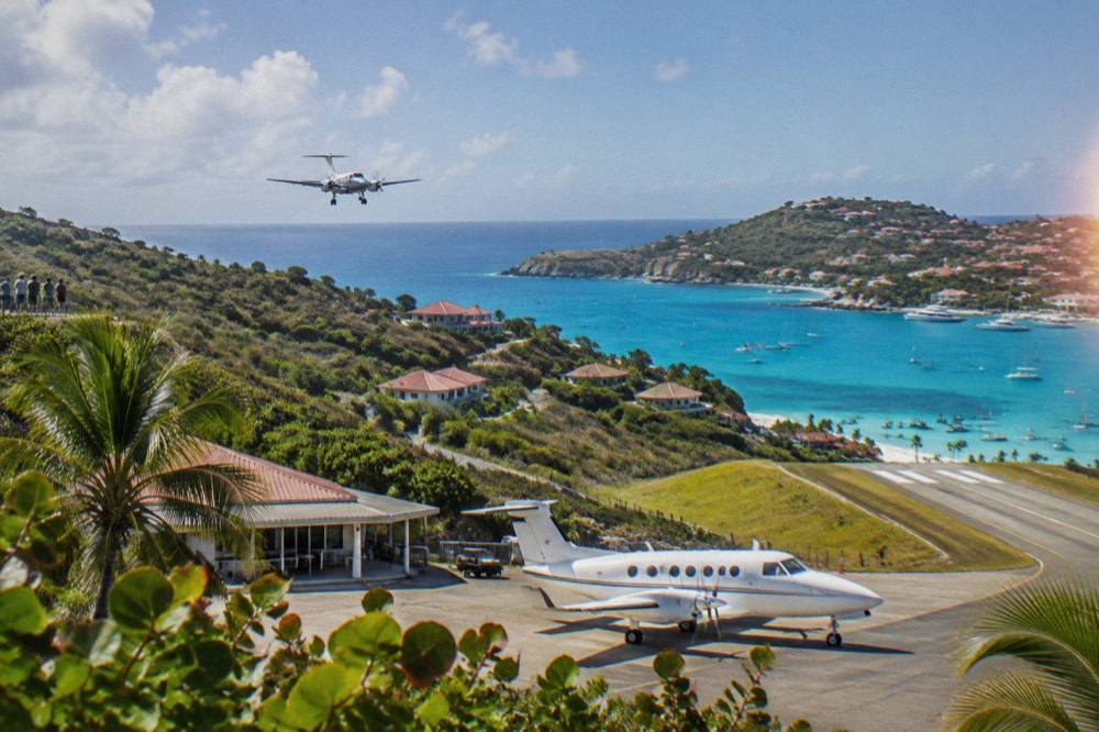 A white Pilatus turboprop parked at a tropical airport terminal under a clear sky