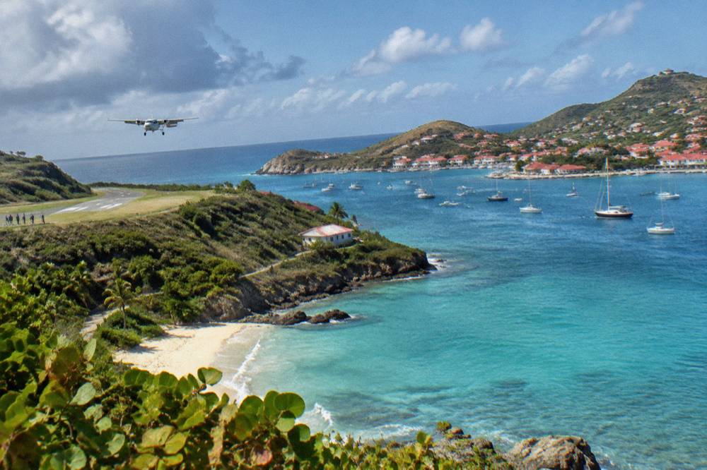An aerial view of a turquoise bay with a town of red roofs and small boats at anchor
