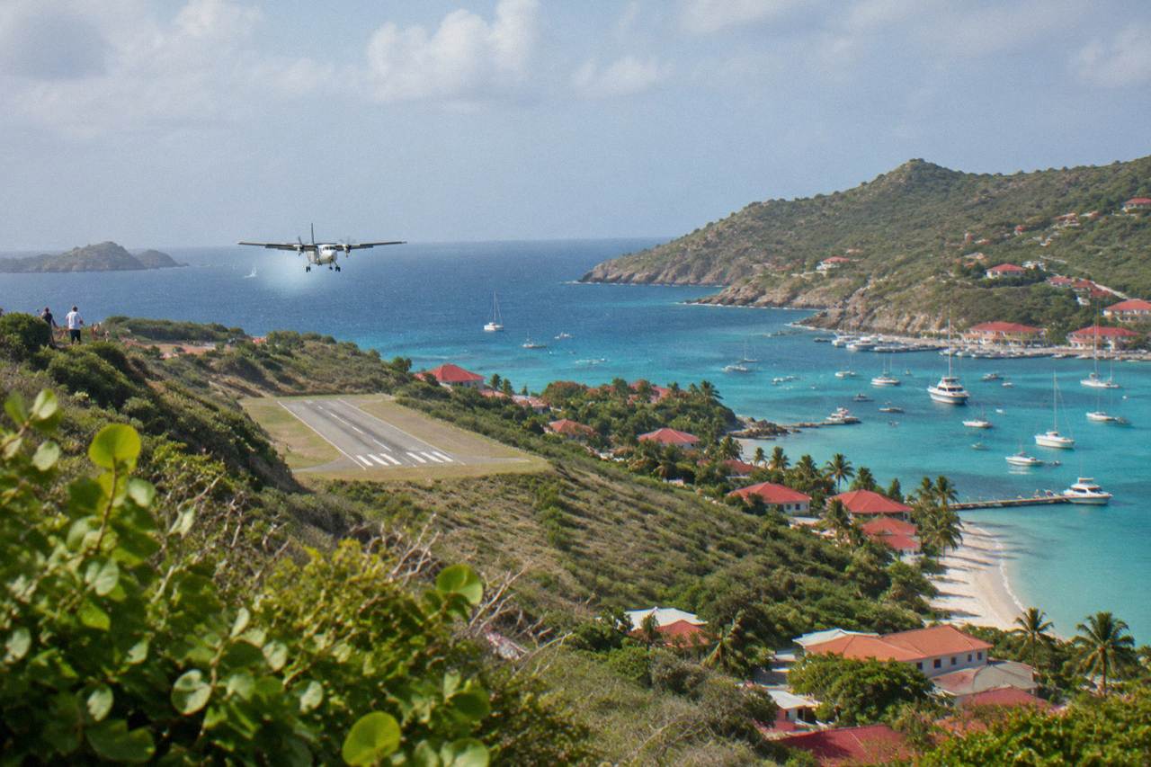 A small turboprop aircraft on a short runway between green hills and turquoise Caribbean water