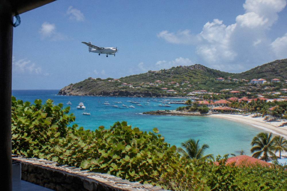 A twin-engine turboprop climbing over turquoise Caribbean water near a green island coast