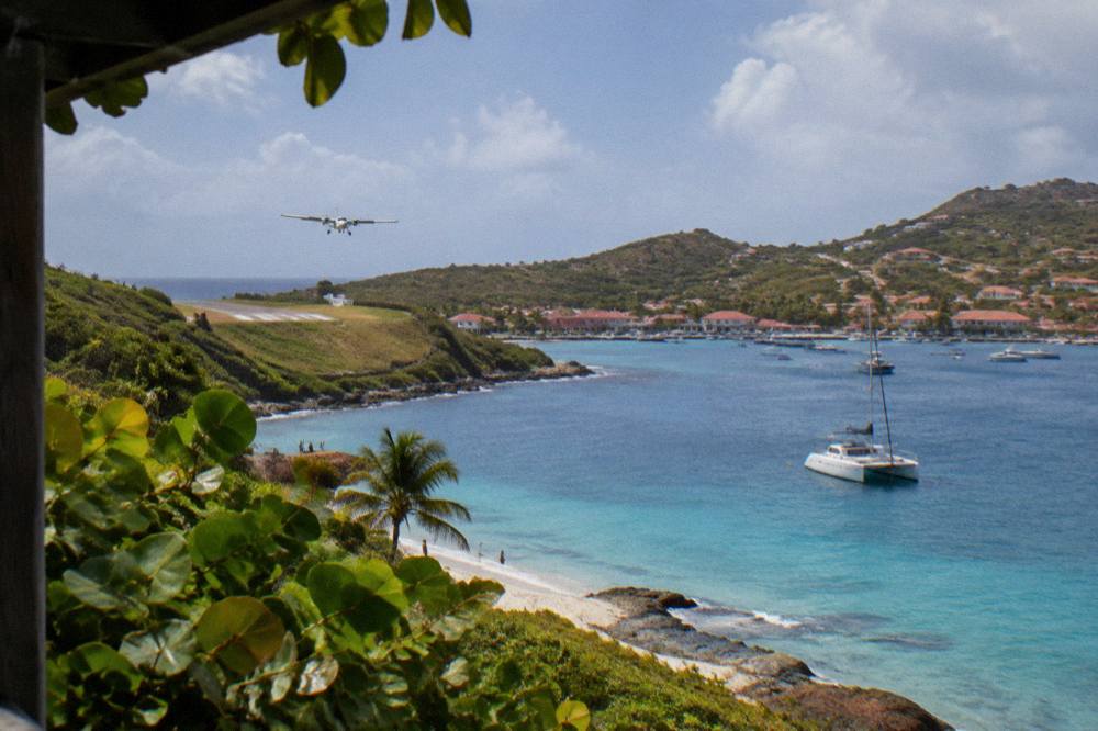 A white catamaran anchored in a calm bay with a hillside village behind
