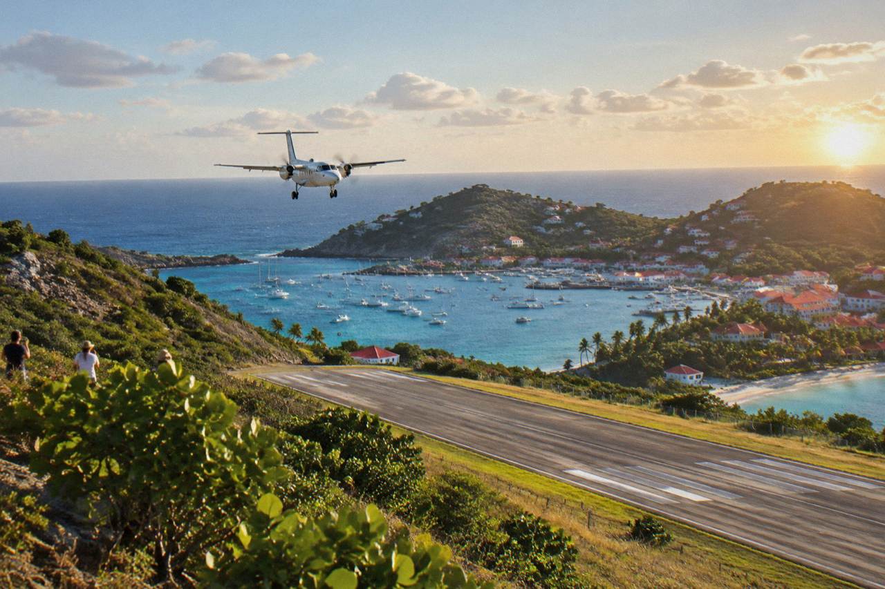 A small turboprop aircraft on a short Caribbean runway with green hills and blue water beyond