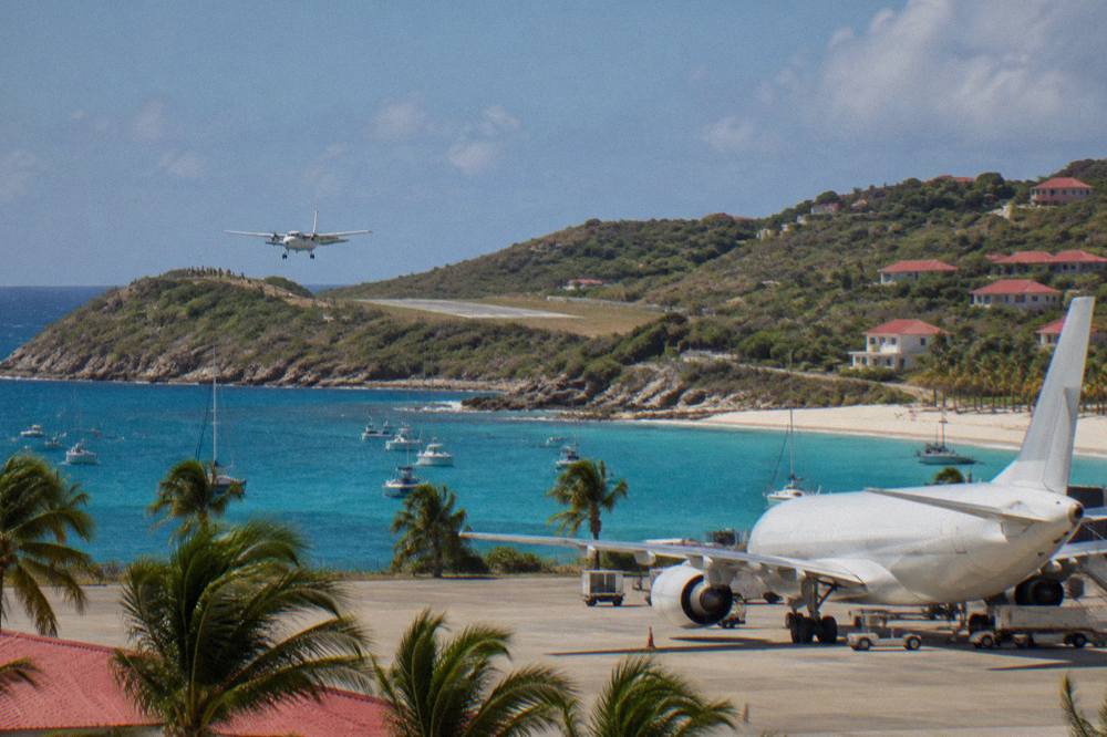 A large jet parked at a sunny Caribbean airport terminal with palm trees