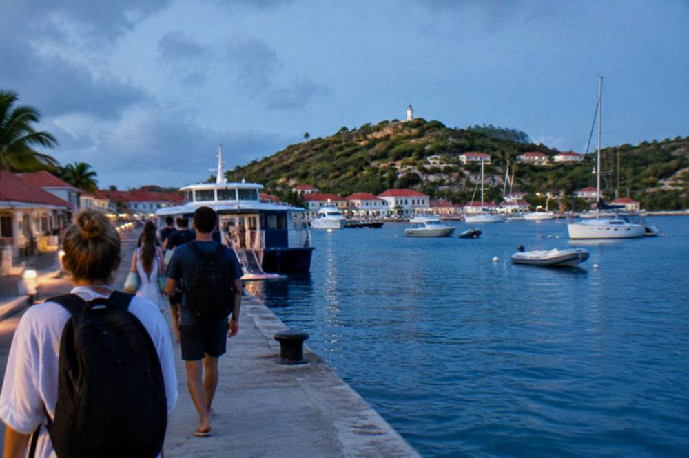 Travellers with day bags walking along a harbour quay toward a moored ferry