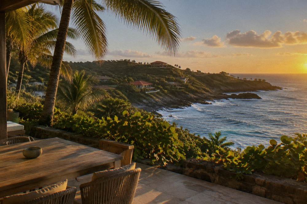 An empty palm-lined terrace in warm evening light on a Caribbean hillside above the sea