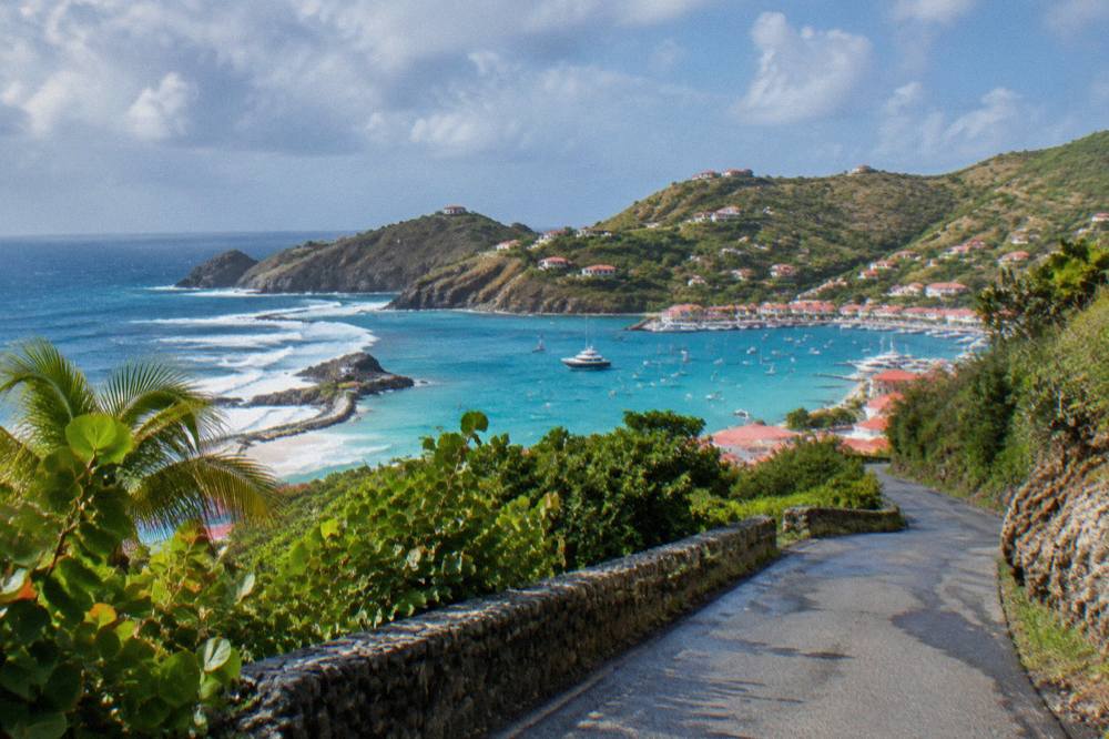 A winding narrow road climbing through green hills toward the sea on a small Caribbean island