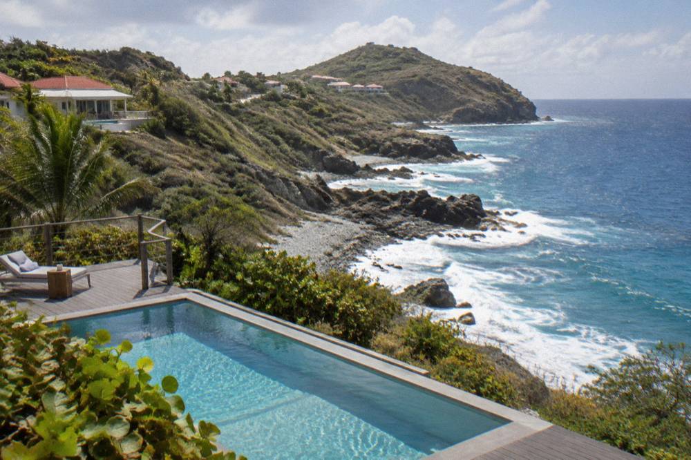 A private plunge pool on a wooden deck overlooking the ocean from a green hillside