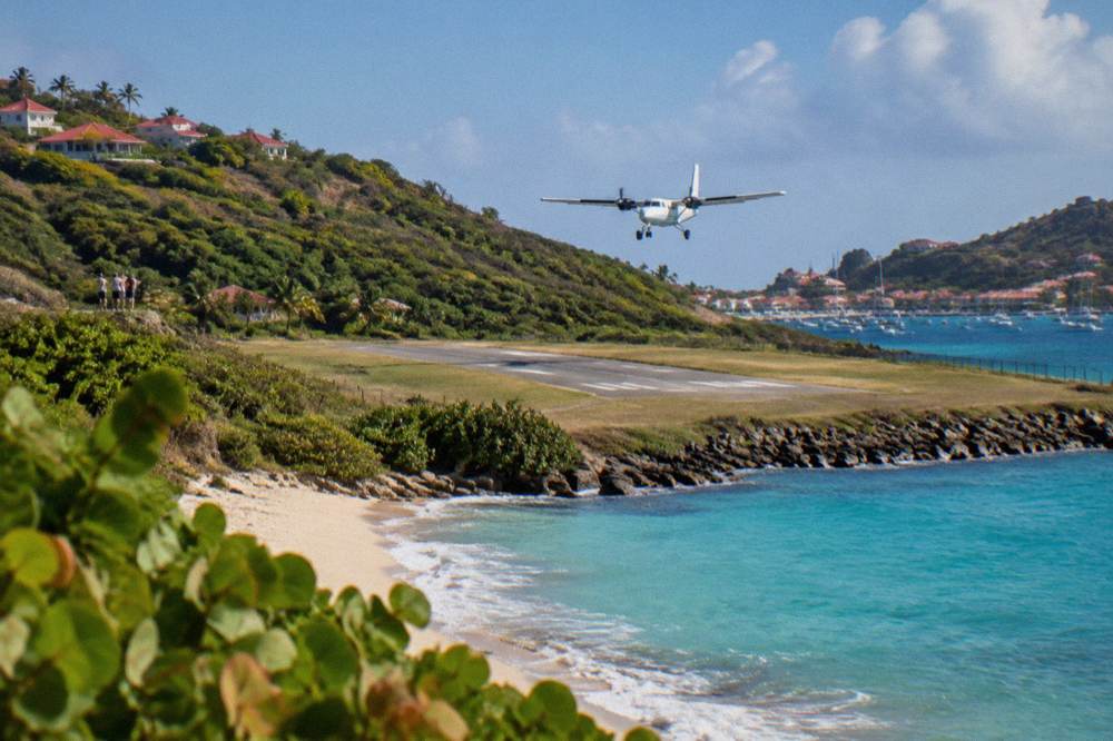 A small twin-engine turboprop airplane on a short runway between a beach and green hills