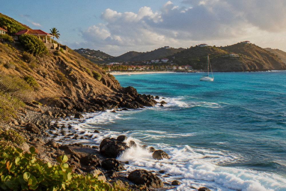A white sailboat anchored in a turquoise bay framed by green headlands