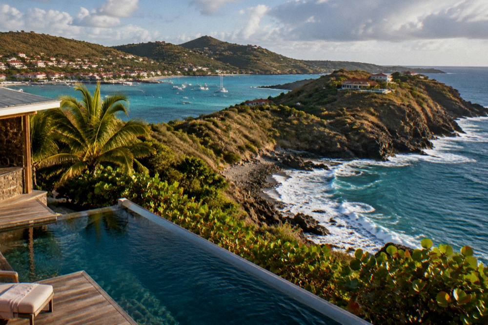 A hillside infinity pool at dusk overlooking a dark sea and a distant coastline