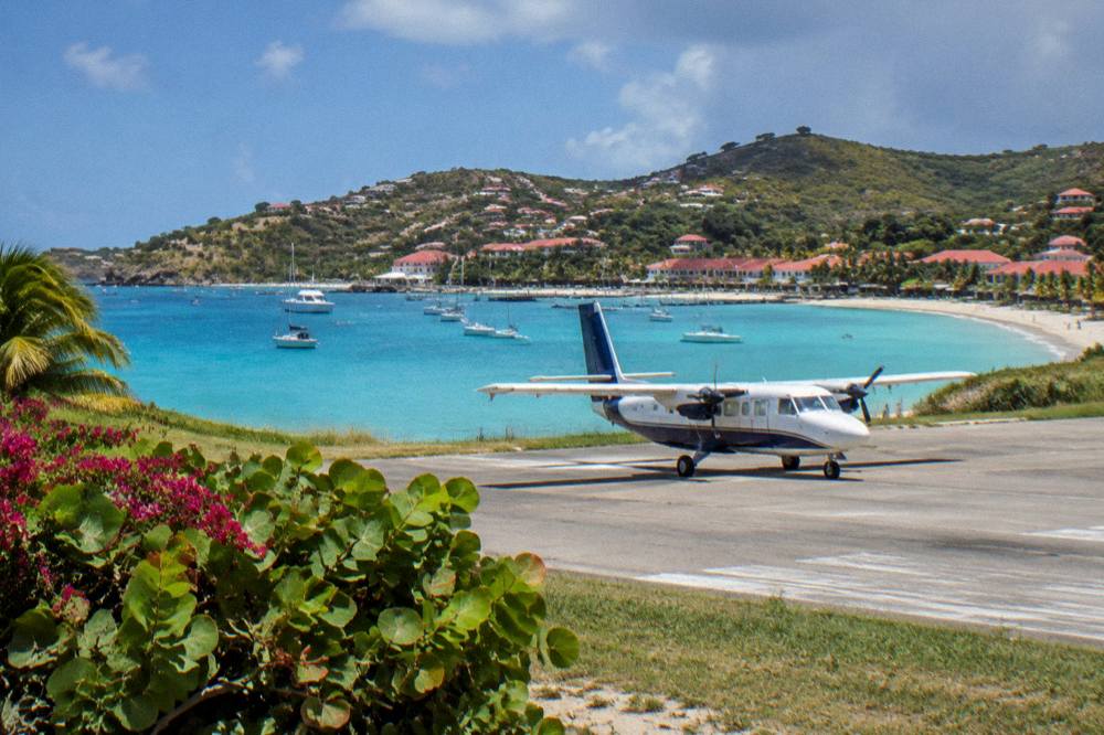 A small twin-engine turboprop parked on a short Caribbean runway beside a beach