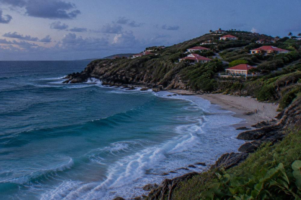 Red-roofed buildings on a green hillside above turquoise Caribbean water