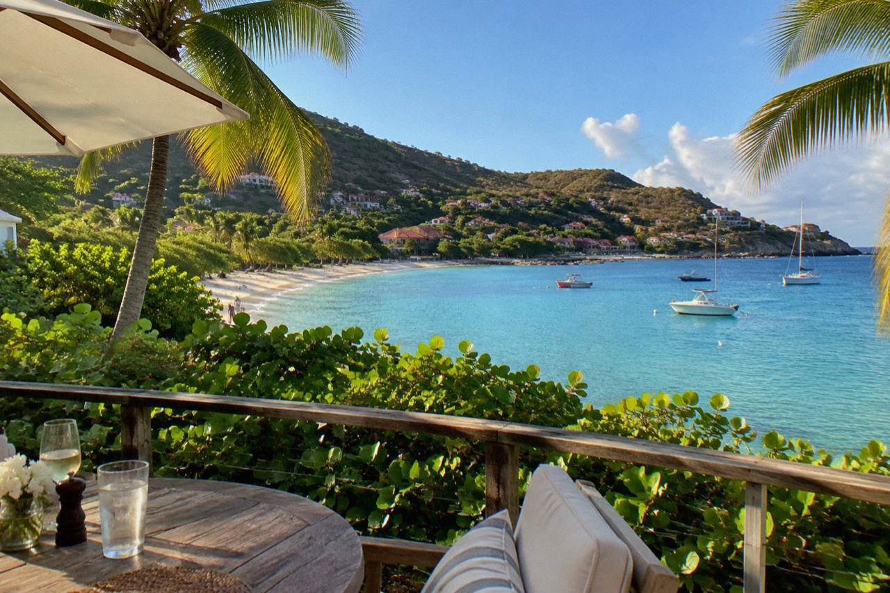 A small hotel terrace overlooking a Caribbean beach with palm trees and turquoise water