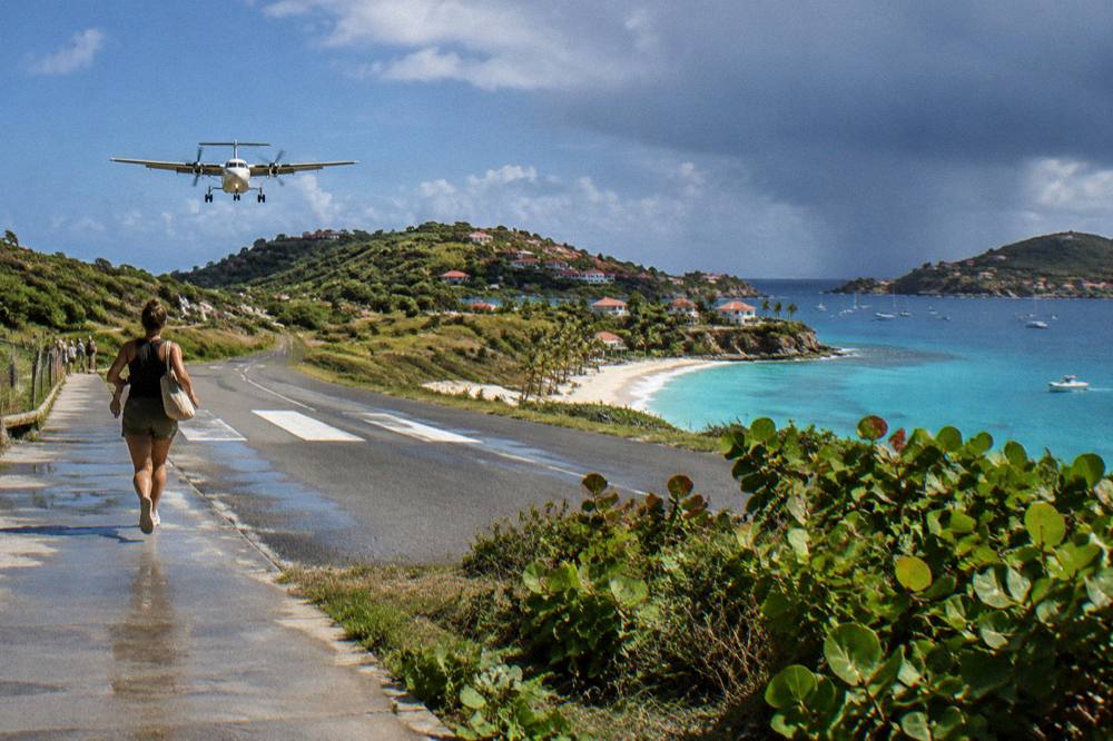 A small turboprop aircraft on a short runway between a hill and a beach