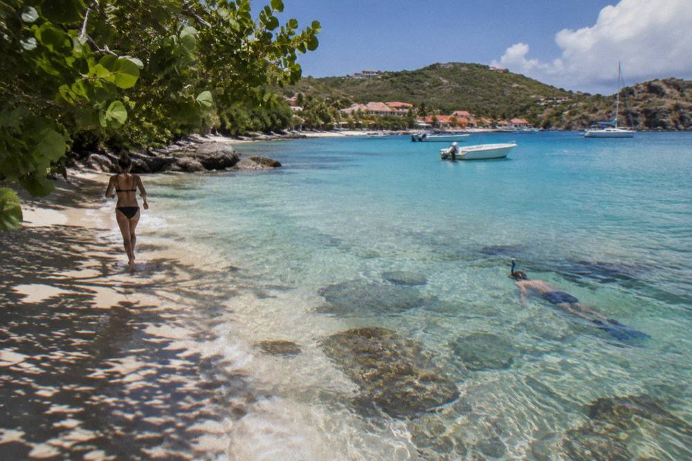 Snorkeler swimming over coral and rocks in clear shallow water