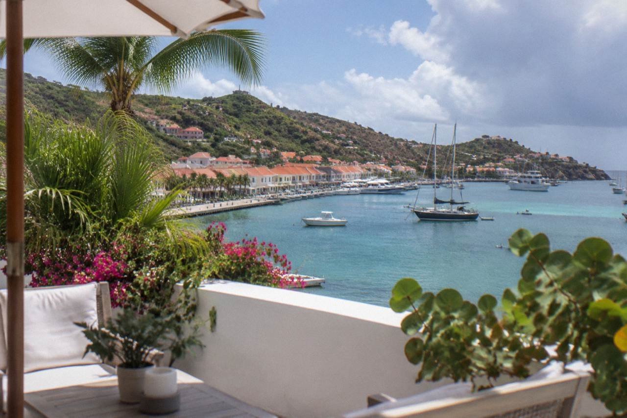 A quiet hotel terrace with white walls and tropical plants near the harbor of a small Caribbean island town