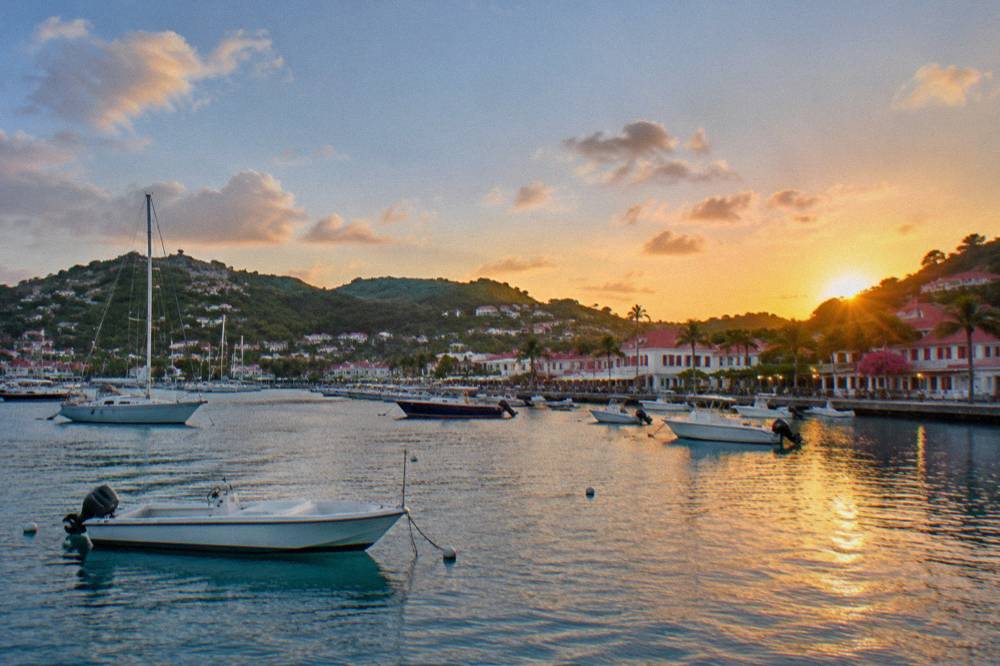 Small boats moored in a Caribbean harbor at dusk with lights reflecting on calm water