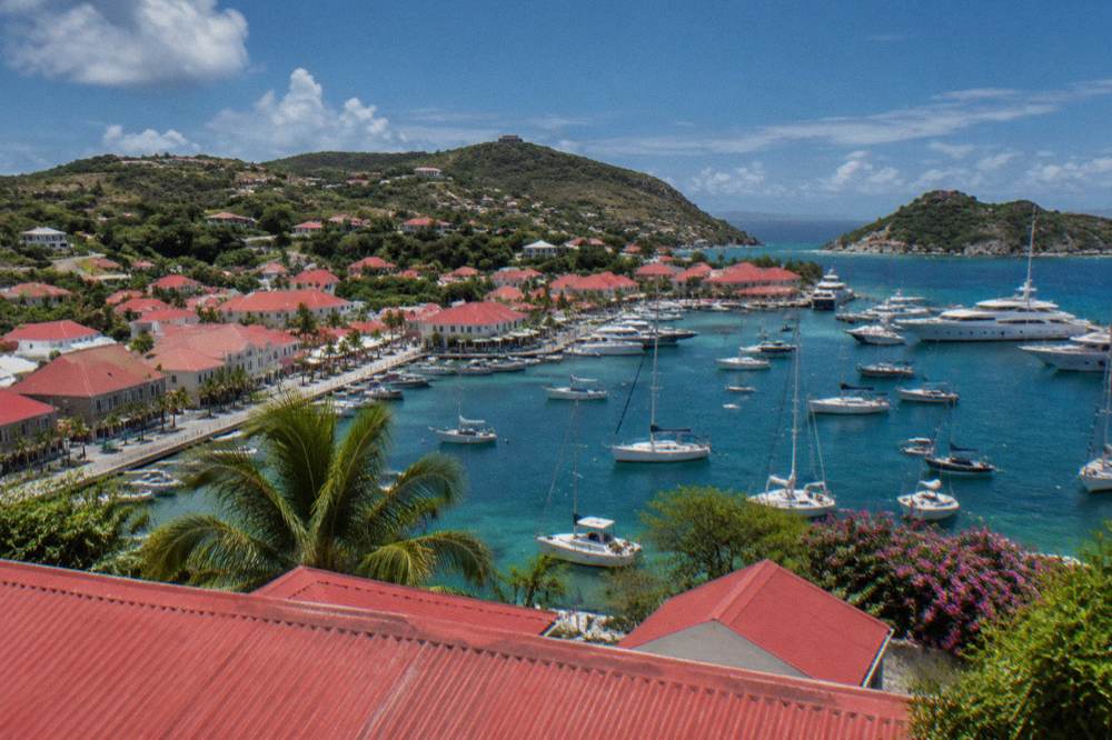 An aerial view of red roofs around a harbor with yachts and green hills beyond