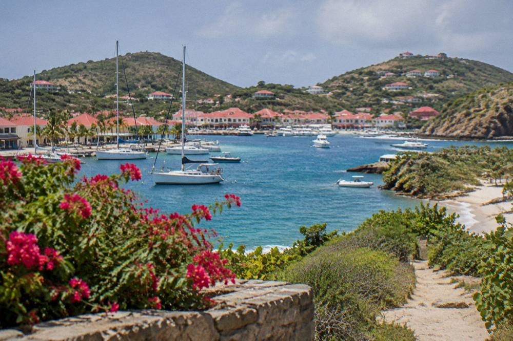 A white sand beach with turquoise water and green headlands, reached by a path through low vegetation