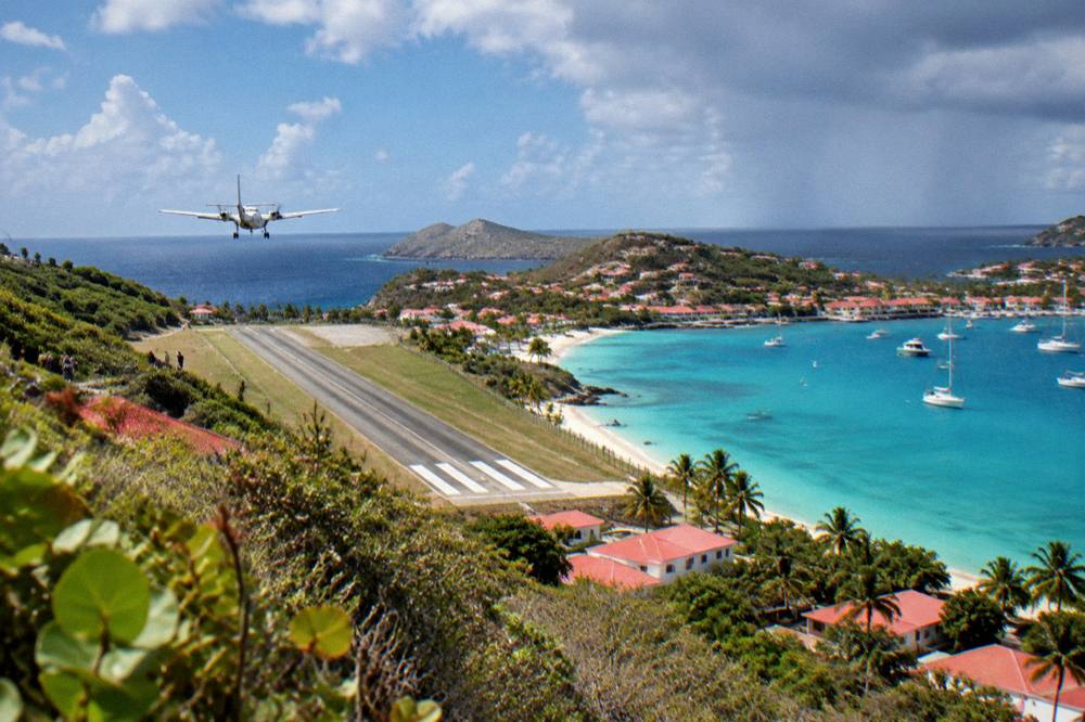 A small turboprop aircraft on a short runway beside a beach and turquoise bay
