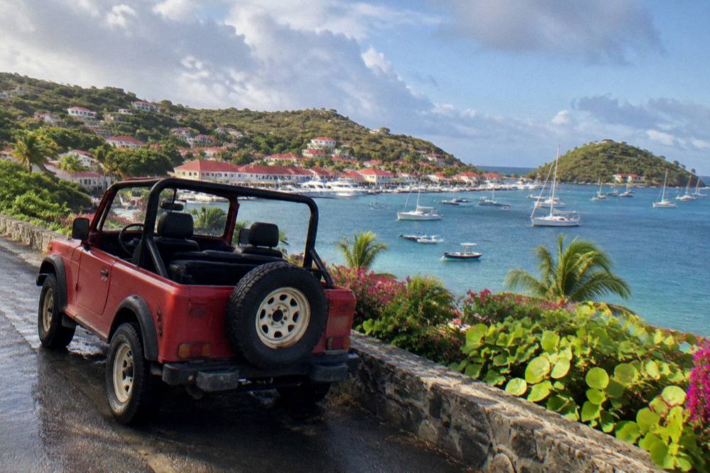 An open-top small jeep parked beside a narrow road with sea view on a green island