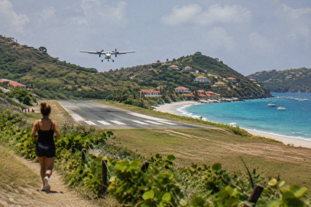 A small turboprop aircraft on a short runway between a hillside and a beach