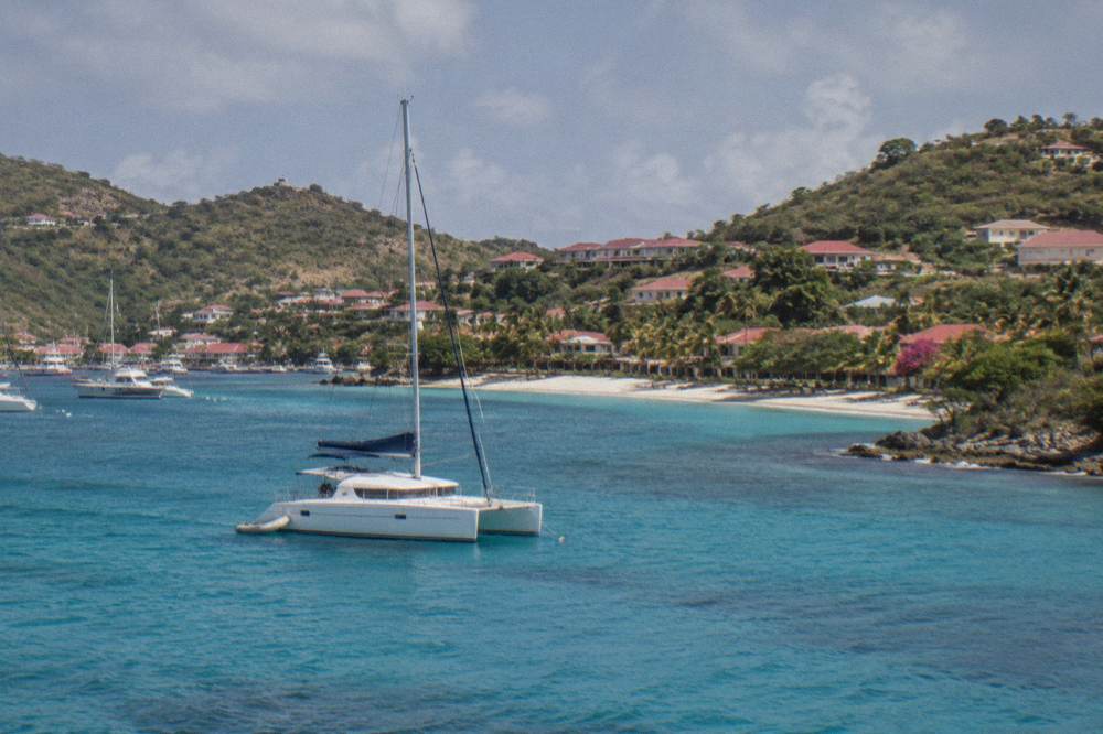A sailing catamaran anchored in a quiet bay with a sandy beach behind it