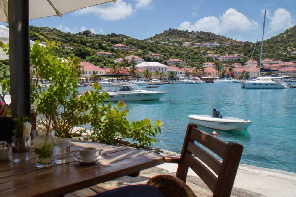An outdoor cafe table beside a harbor with white boats moored in clear water