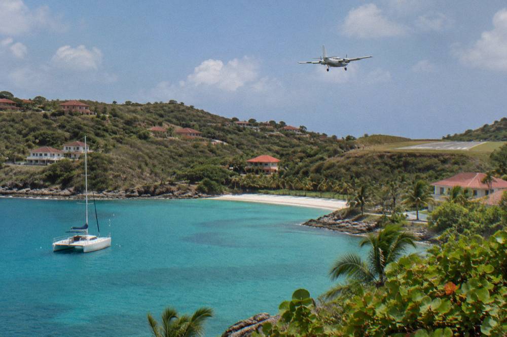 A white catamaran anchored in a quiet green bay with a wooded hill behind it
