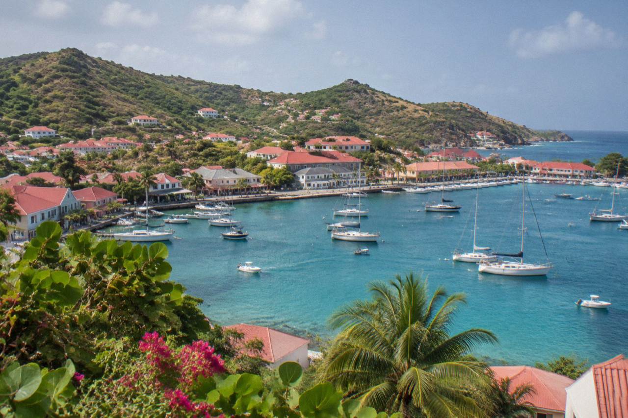 Aerial view of a small Caribbean island with red roofs around a harbor and turquoise water