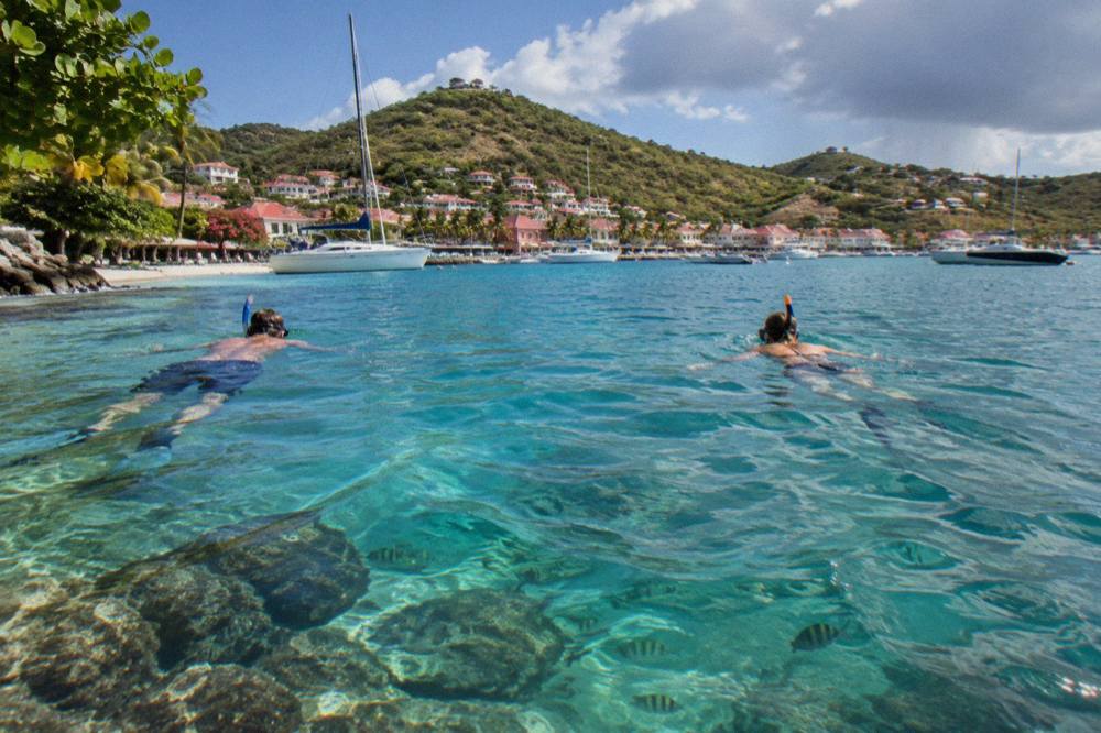 Snorkellers floating over clear shallow water above rocks and small fish