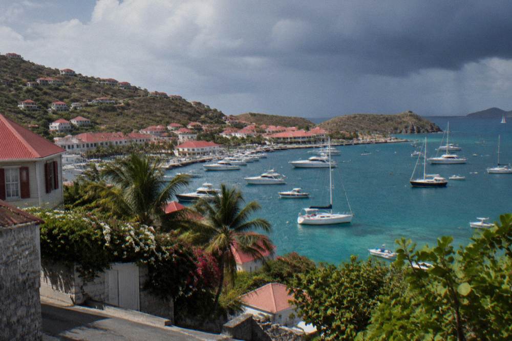 Dark storm clouds gathering over a turquoise Caribbean bay with palm trees along the shore