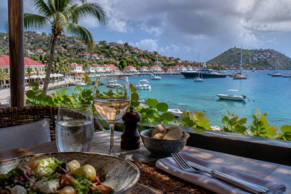 A table set for lunch on a shaded terrace overlooking a bright Caribbean bay