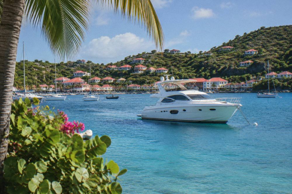 A white motor yacht anchored in a clear blue bay with a wooded hill behind it