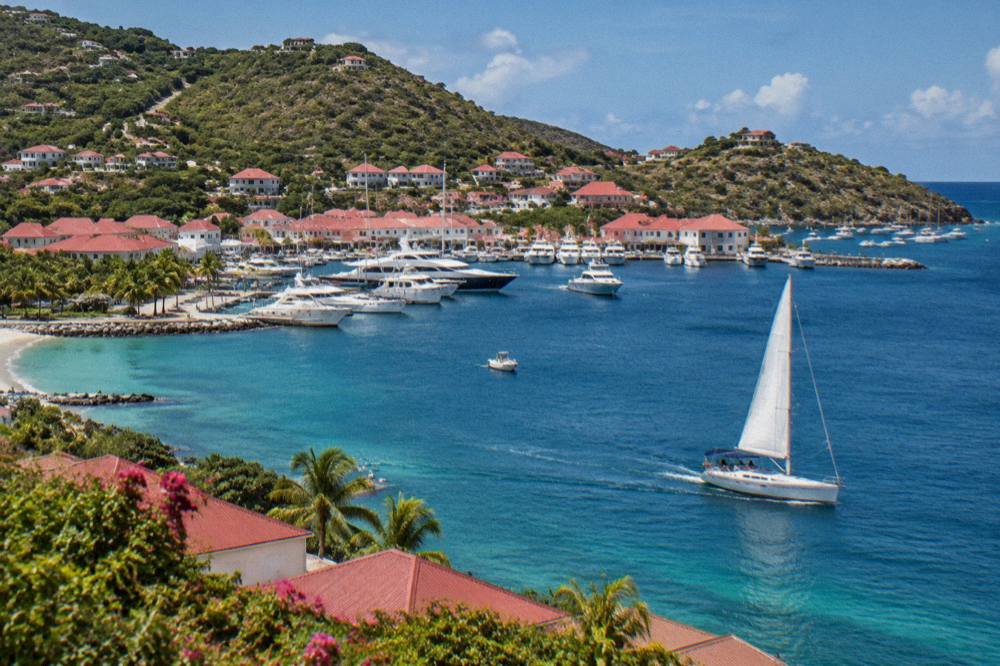 A sailboat under way on open blue water with crew on deck and distant green hills