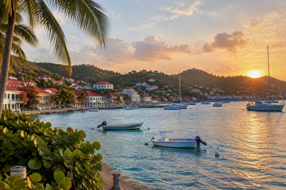 Sunset light over red rooftops and a harbour with boats at anchor along a Caribbean shoreline