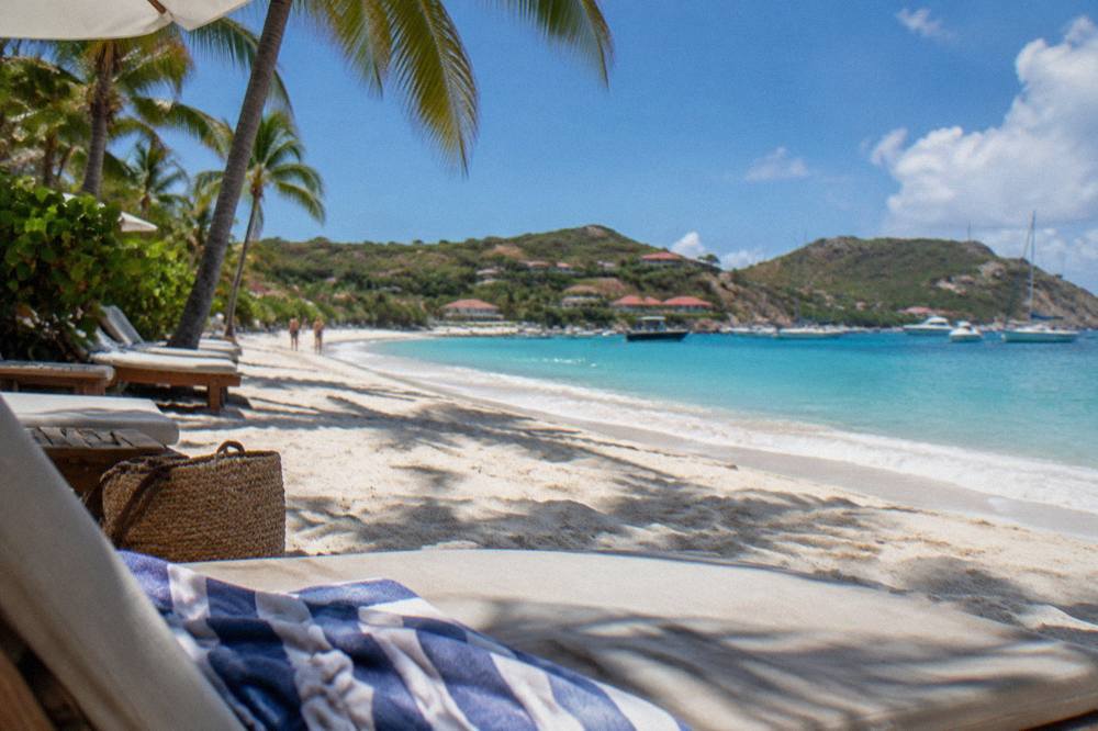 Sun loungers and palm shade at the edge of a wide sandy beach in the Caribbean