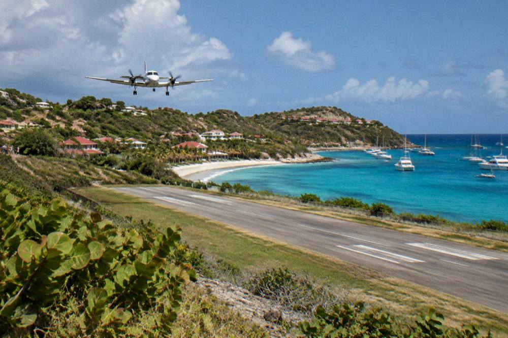 A small turboprop aircraft on a short runway beside a beach and green hills