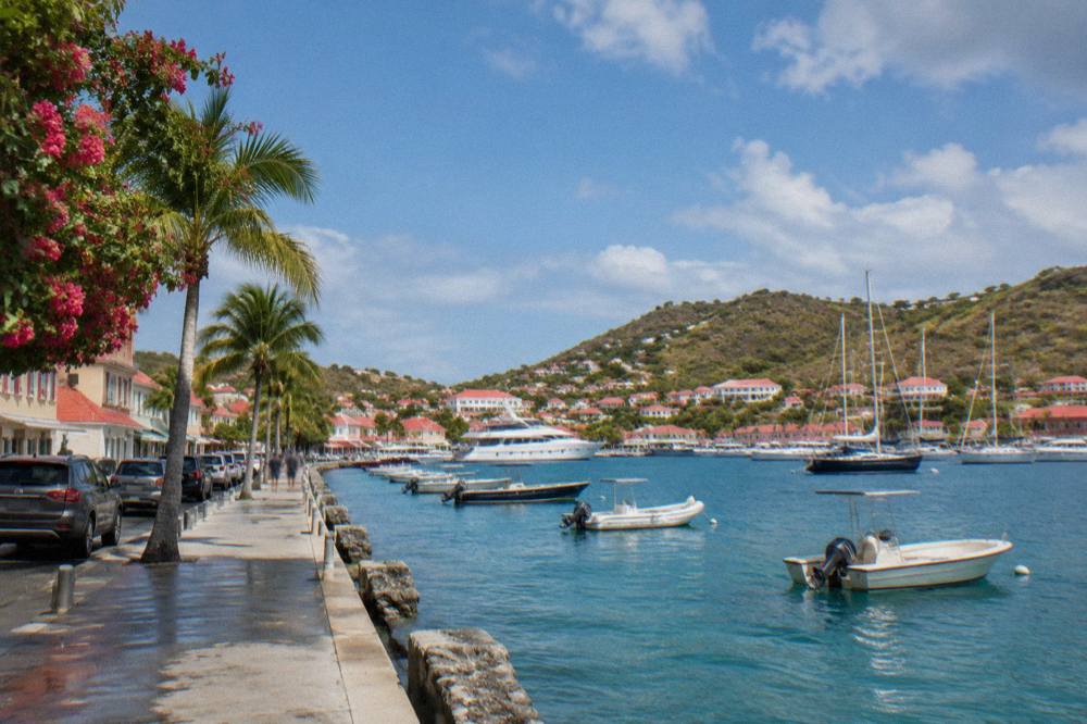 Waterfront street in Gustavia with storefronts and parked cars along the harbor road
