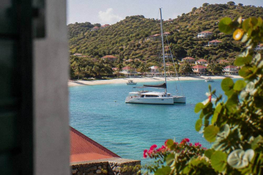 Catamaran moored in a clear turquoise bay with a sandy beach and green hillside in St Barts